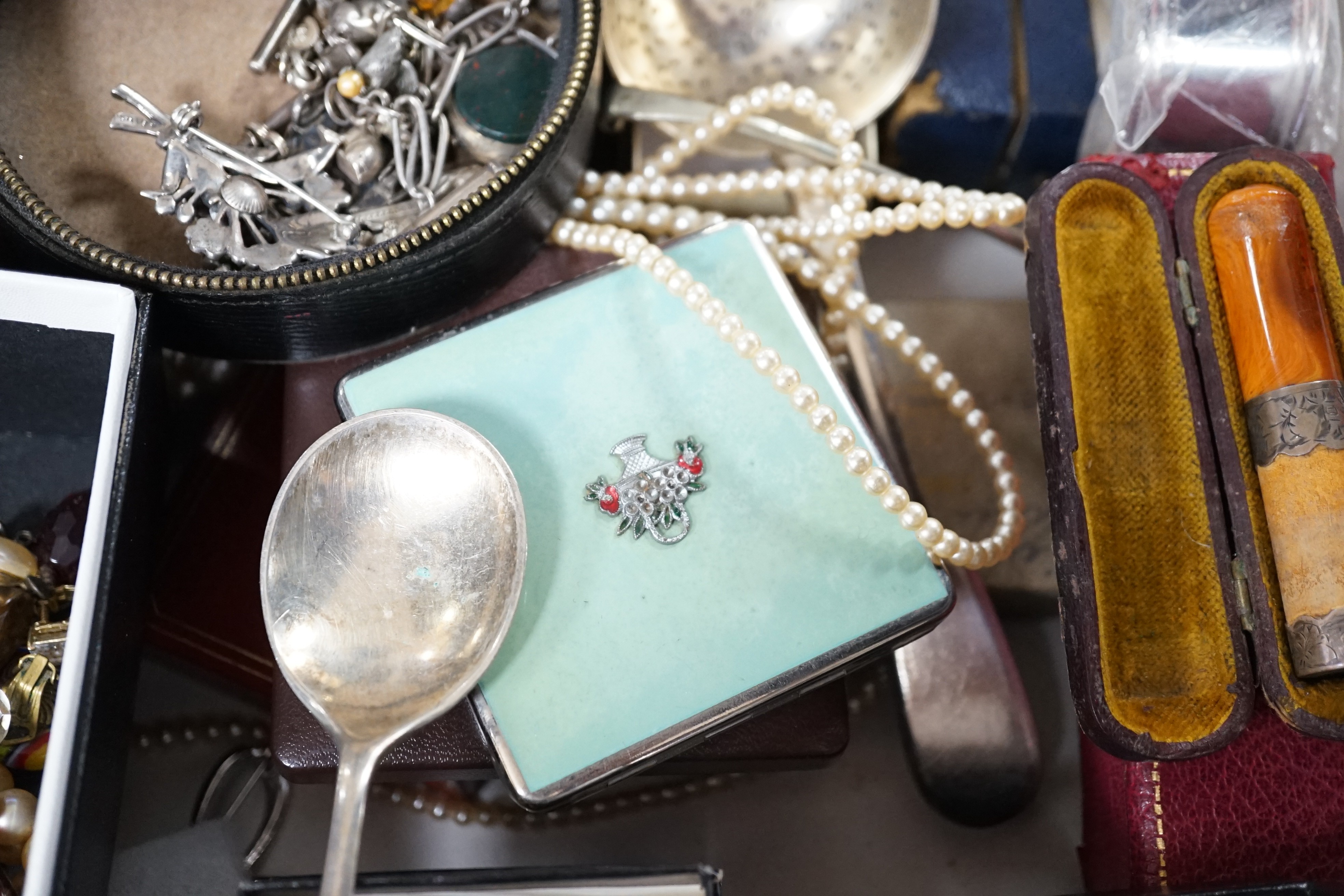 A collection of assorted jewellery including costume, silver and enamel flower head brooch, silver mounted amber cigarette holder, plated flatware, necklaces, commemorative coin, Victorian silver locket, white metal brac